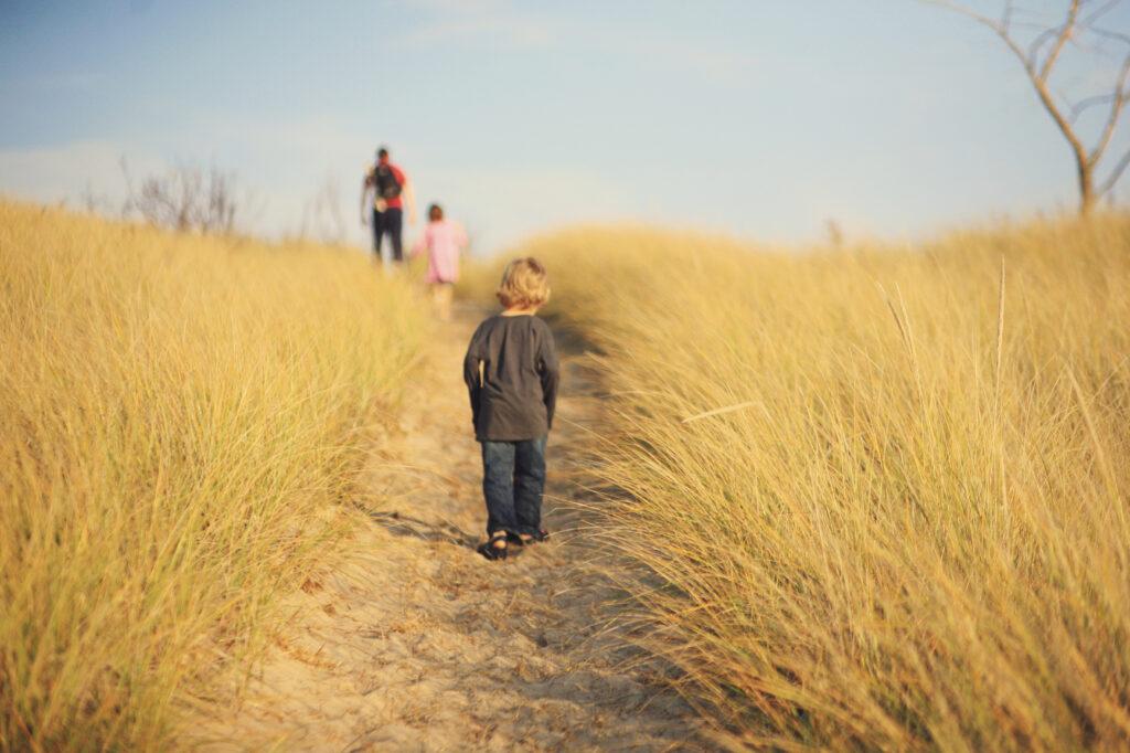 Little boy and his family walking along a sandy path near Lake Michigan