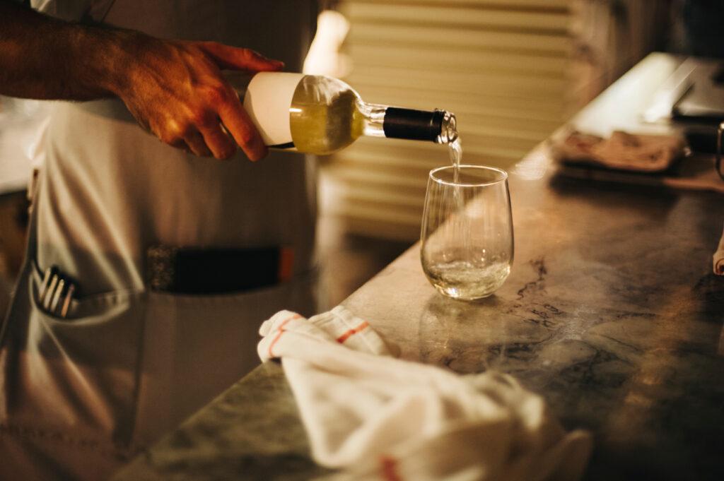 An anonymous server pouring a glass of wine to be served to a guest at a restaurant.